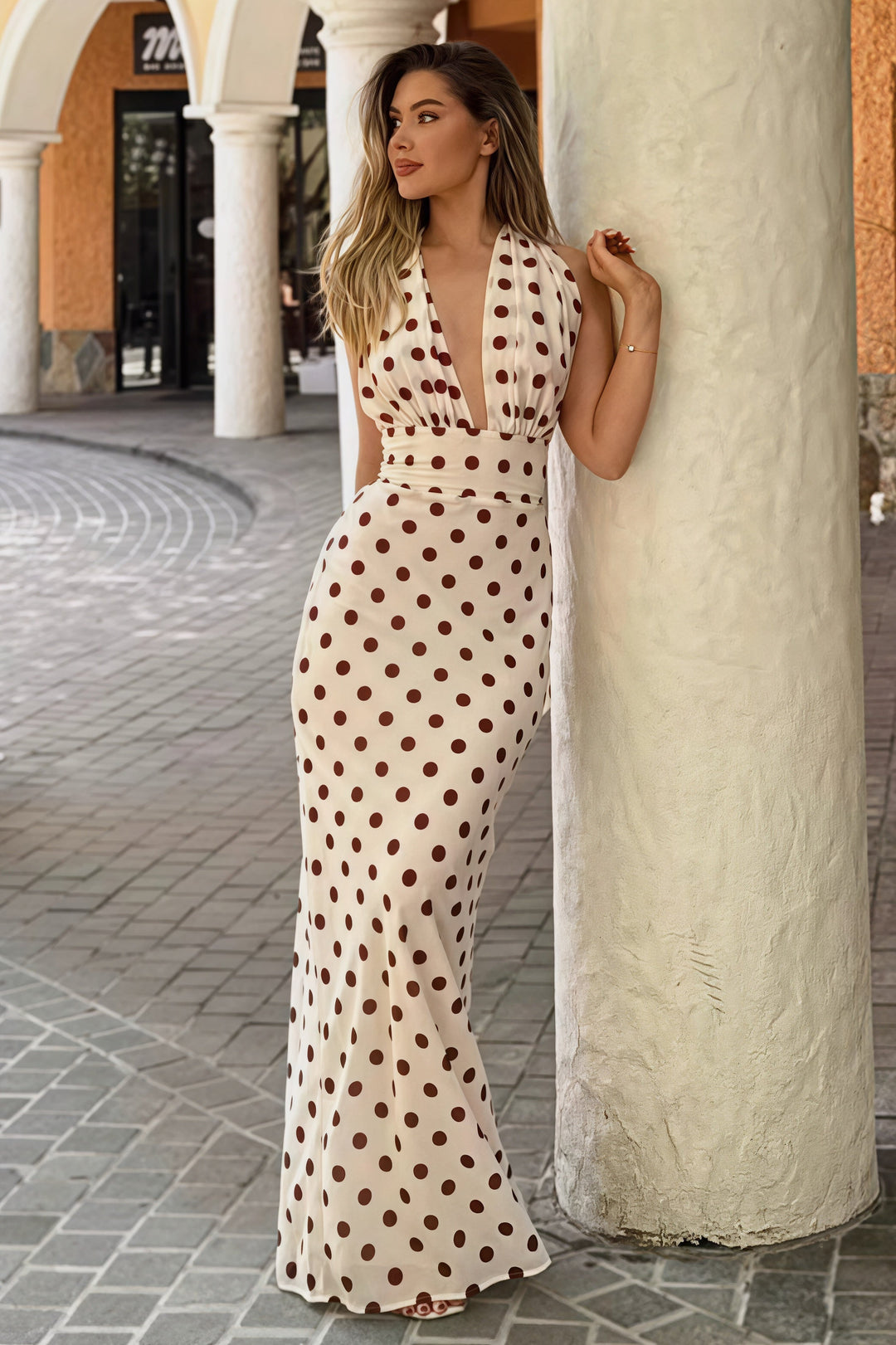 The Amalfi Polka Dot Maxi — cream halterneck maxi dress with bordeaux polka dots, styled in a Mediterranean setting.